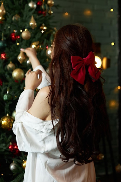 La donna decora un albero di Natale con ghirlande e giocattoli a casa Mattina prima di Natale Capodanno 2023