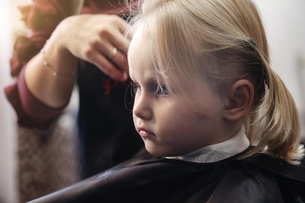 La donna del barbiere fa una bella acconciatura alla moda per una bambina carina