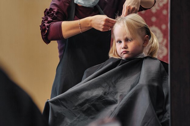 La donna del barbiere fa una bella acconciatura alla moda per una bambina carina