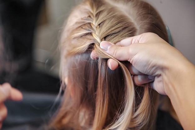 La donna del barbiere fa una bella acconciatura alla moda per una bambina carina