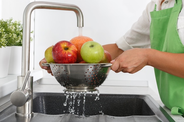 La donna del cuoco lava i frutti sotto l'acqua corrente da un rubinetto dell'acqua.