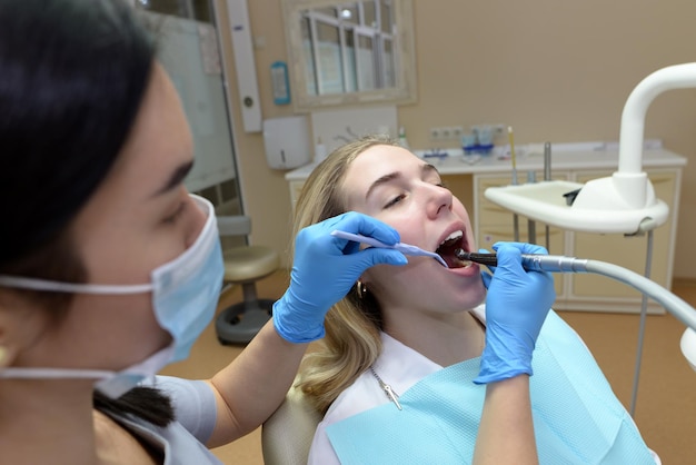 La donna del dentista tratta i denti di un giovane paziente con l'aiuto di strumenti dentali professionali Il cliente si trova sulla poltrona del dentista