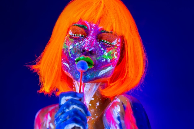 La donna del modello di moda lecca le caramelle dolci alla luce al neon, night-club della discoteca. Trucco fluorescente luminoso variopinto della bella ragazza di modello