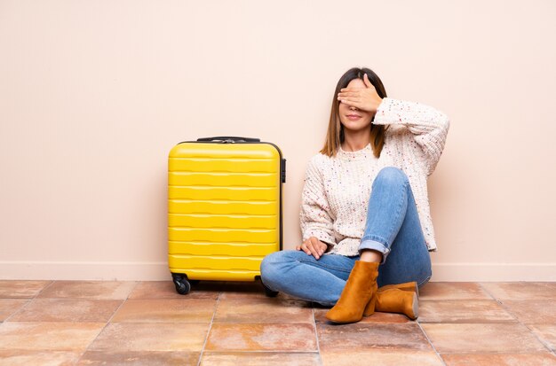 La donna del viaggiatore con la valigia che si siede sul rivestimento del pavimento osserva a mano