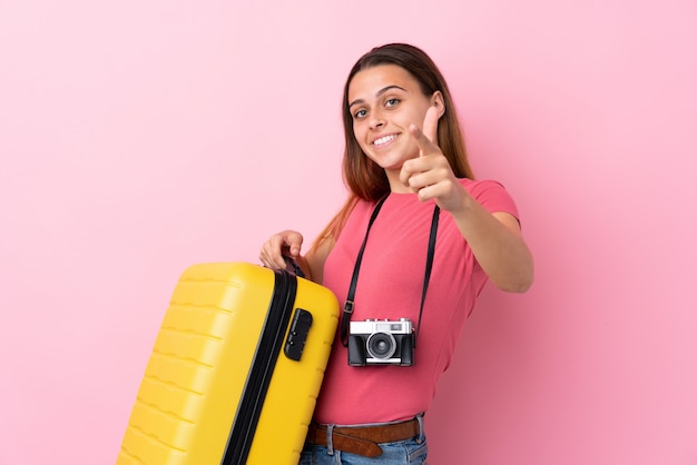 La donna del viaggiatore dell'adolescente che tiene una valigia sopra la parete rosa isolata indica il dito voi con un'espressione sicura