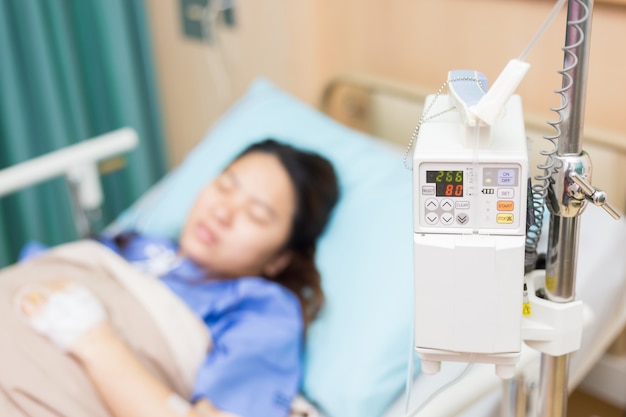 La donna dell&#39;Asia pazienta con la macchina automatica della soluzione di infusione IV nella stanza paziente
