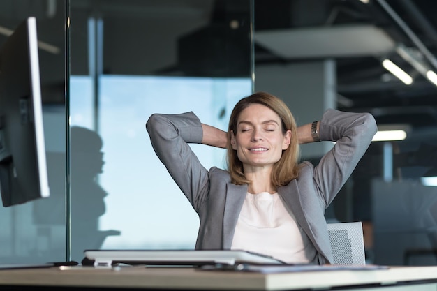 La donna dell'imprenditore che riposa durante l'orario di lavoro mette le mani dietro la testa e pensa ai piani aziendali che lavorano in un ufficio moderno