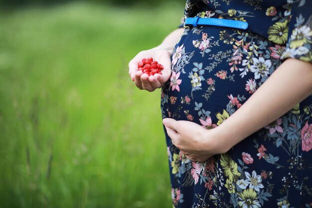 La donna della camicia bianca che tiene molte fragole fresche nelle sue mani con lo sfondo verde della natura. Condivisione di fragole fresche dal giardino.