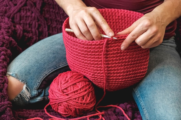 La donna delle mani in un ambiente domestico accogliente lavora a maglia da un filo rosa. Copia, spazio vuoto per il testo.