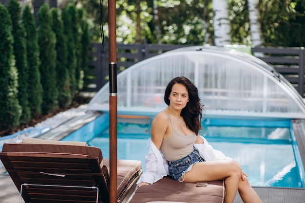 La donna dello stile di vita del giorno d'estate si rilassa e si rilassa vicino alla lussuosa piscina per prendere il sole presso il resort sulla spiaggia all'aperto l'hotel Vacanze e concetto estivo