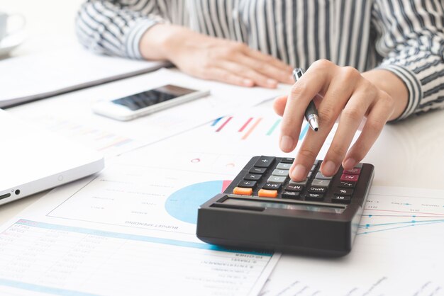 La donna di affari che utilizza la calcolatrice e la scrittura prende nota con il calcolo. tasse e concetti economici.