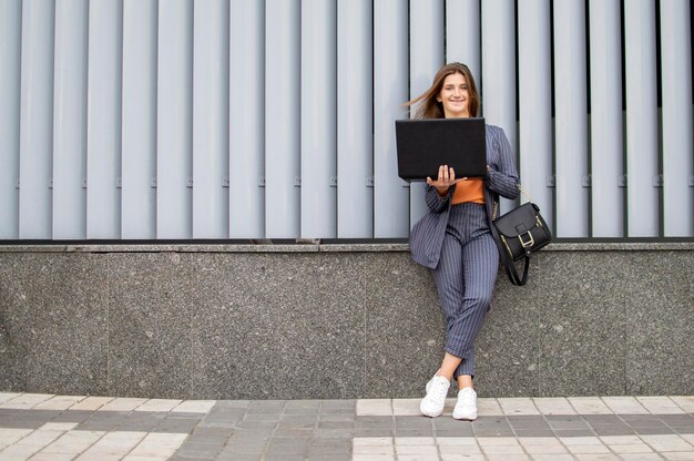 La donna di affari con il computer portatile rimane in città sullo sfondo del muro