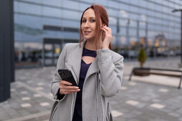 La donna di affari dai capelli rossi adulta parla su un telefono cellulare tramite le cuffie sullo sfondo di a