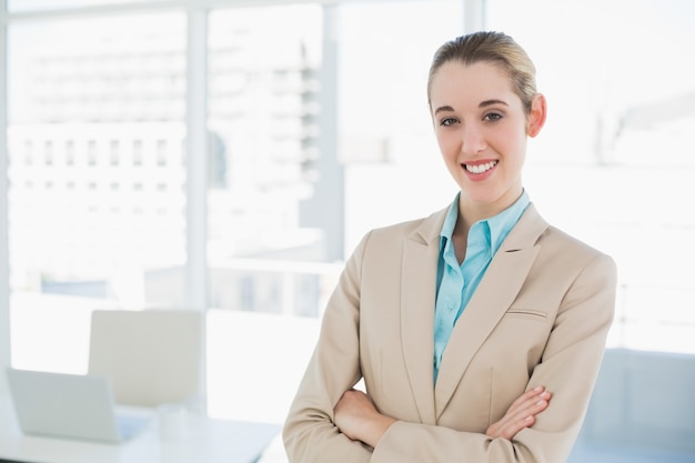 La donna di affari elegante sorridente adorabile che posa con le armi ha attraversato sorridere alla macchina fotografica