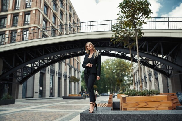 La donna di affari in un vestito nero cammina attraverso la città di estate.