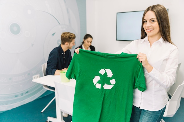 La donna di affari sorridente che mostra la maglietta verde con ricicla il simbolo