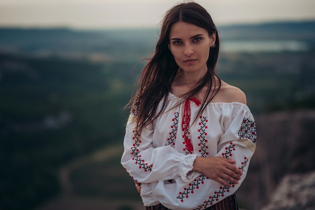 La donna di Atractive in costume rumeno tradizionale su verde della montagna ha offuscato il fondo