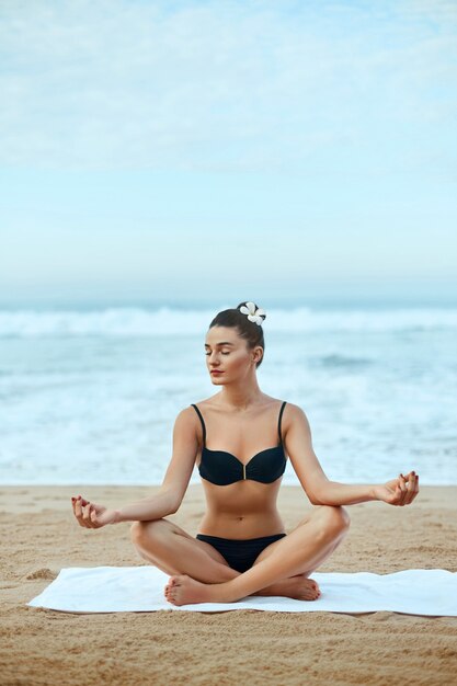 La donna di bellezza pratica lo yoga e medita nella posizione del loto sulla spiaggia. Meditazione. Stile di vita attivo. Concetto sano e yoga. Fitness e sport