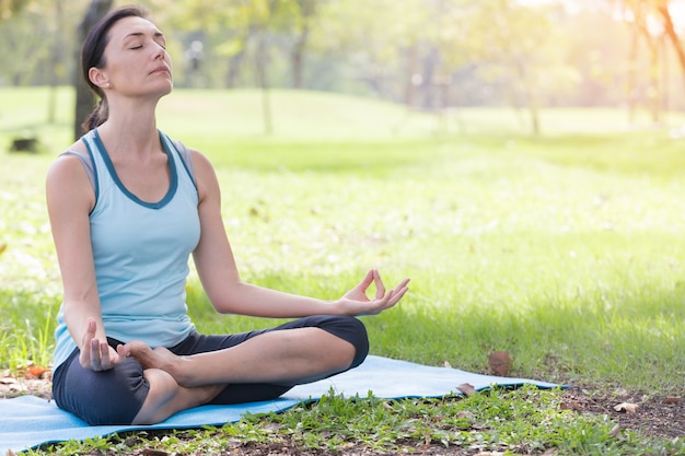 La donna di festa che fa la meditazione di posa di yoga nel parco pubblico mette in mostra il concetto sano.