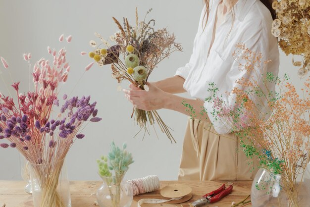 La donna di media altezza che lavora con i fiori secchi assembla la decorazione della composizione e il concetto di floristica