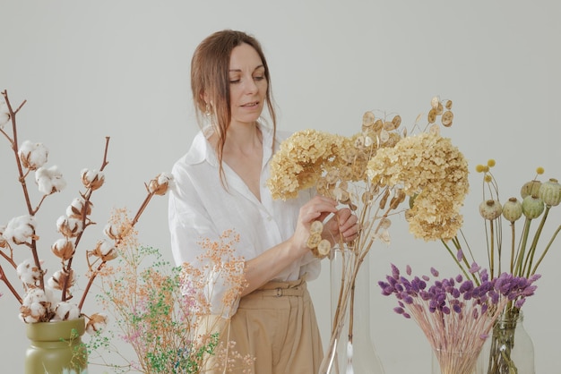 La donna di media altezza che lavora con i fiori secchi assembla la decorazione della composizione e il concetto di floristica