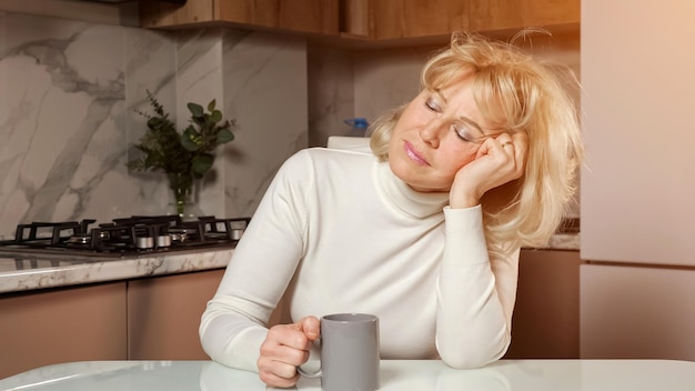 La donna di mezza età assonnata beve il caffè seduto in cucina