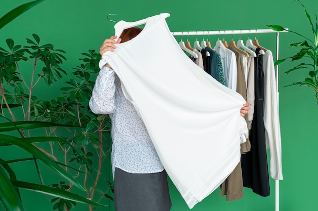 La donna di mezza età fa shopping e guarda il nuovo vestito vicino allo scaffale con i vestiti.