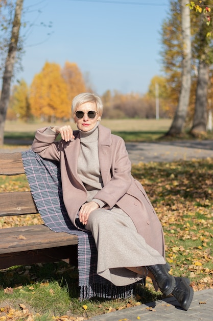 La donna di mezza età si siede su una panchina del parco in autunno. Foto di alta qualità