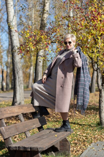 La donna di mezza età si siede su una panchina del parco in autunno