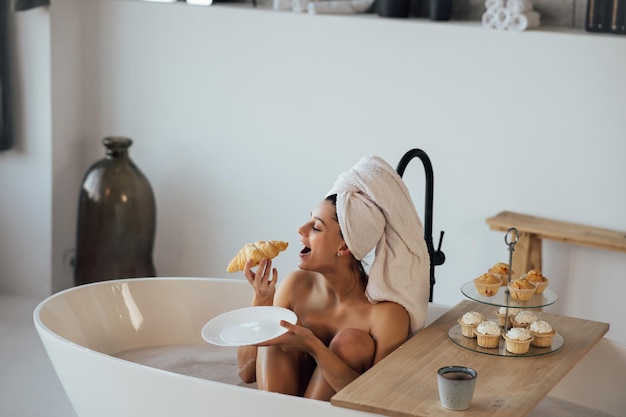 La donna di moda di lusso al mattino fa colazione sdraiata nella vasca da bagno