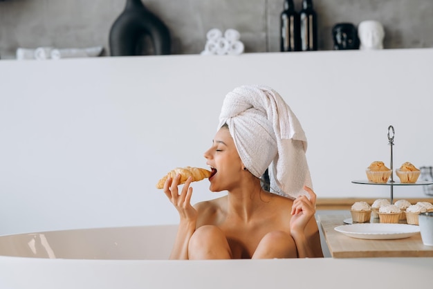 La donna di moda di lusso al mattino fa colazione sdraiata nella vasca da bagno