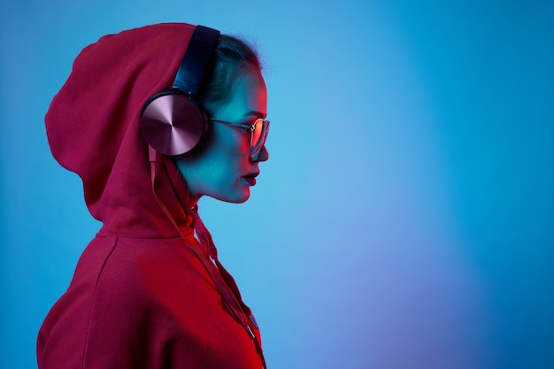 La donna di moda hipster indossa occhiali alla moda e cuffie che ascoltano musica su sfondo al neon di colore in studio.