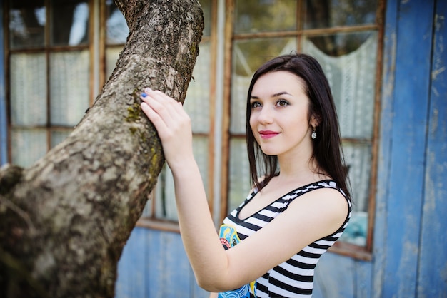 La donna di modello del Brunette al vestito con le bande ha proposto vicino all'albero.