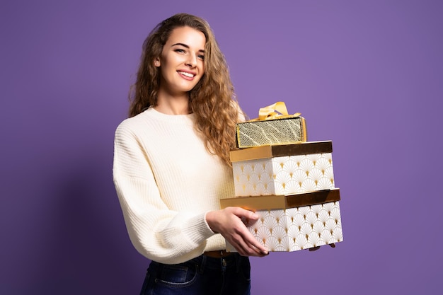 La donna di Natale in un posto bianco tiene molte scatole regalo su sfondo viola per studio concetto di natale...