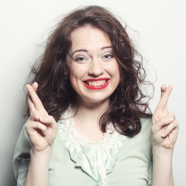 La donna di smiley che spera duro con le dita ha attraversato contro la parete grigia