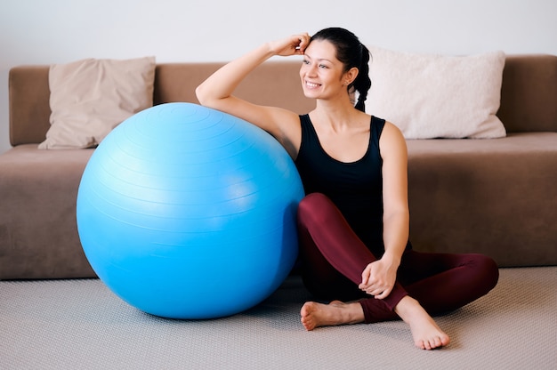 La donna di sport nella seduta degli abiti sportivi si rilassa e fa l'esercizio di forma fisica con la testa di legno e il fitball blu