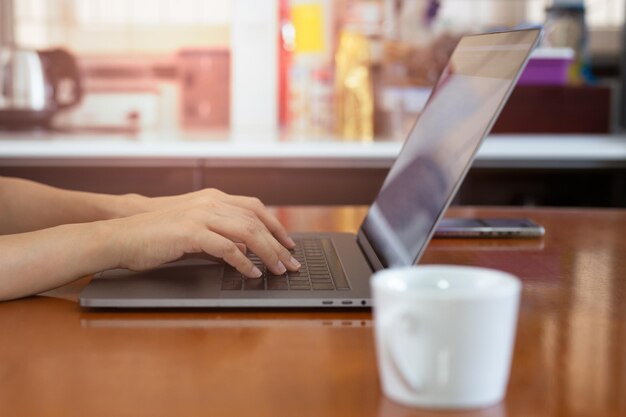La donna digita sulla tastiera del laptop seduto sul tavolo vicino alla finestra di casa