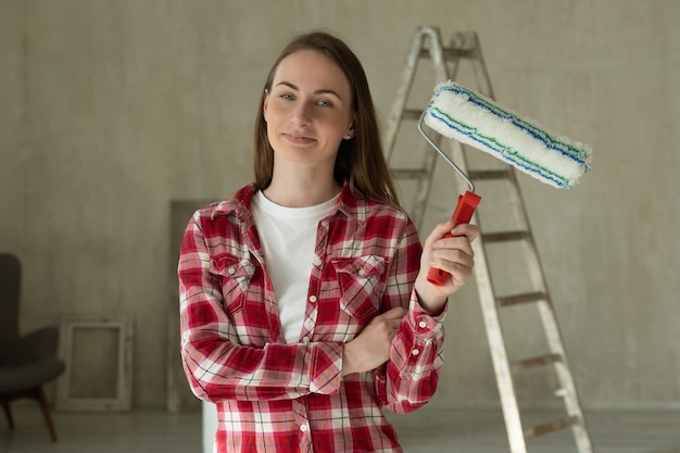 La donna dipinge le pareti a casa tiene la riparazione del rullo e il concetto di ristrutturazione della casa