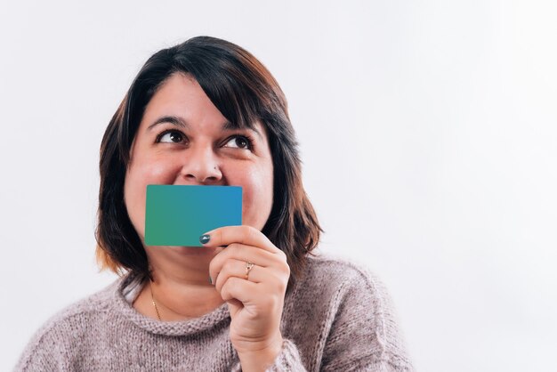 La donna divertente guarda di lato e un sorriso è coperto da una carta di credito che la rende felice. Concetto di acquisto online o su Internet. Copia spazio