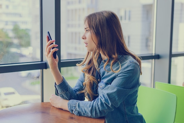 La donna è delusa a causa degli sms che ha ricevuto dalla sua amica. Sta guardando il suo telefono cellulare con la bocca aperta e la tristezza.