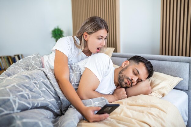 La donna è gelosa e sospettosa e spia nello smartphone del compagno mentre lui dorme in camera da letto La moglie spia il telefono del marito mentre lui dorme Il concetto di sfiducia gelosia