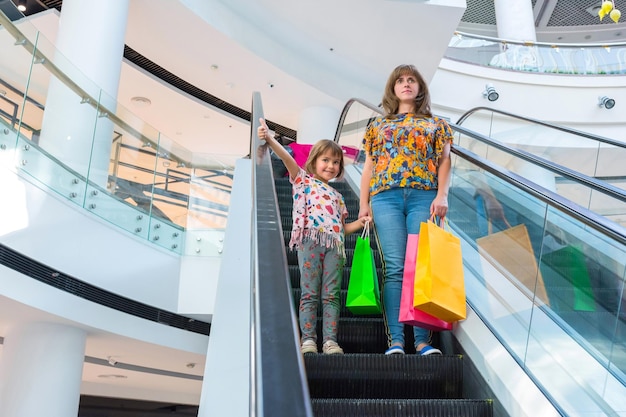 La donna e il bambino felice con i pacchi sulla scala mobile nel negozio del centro commerciale