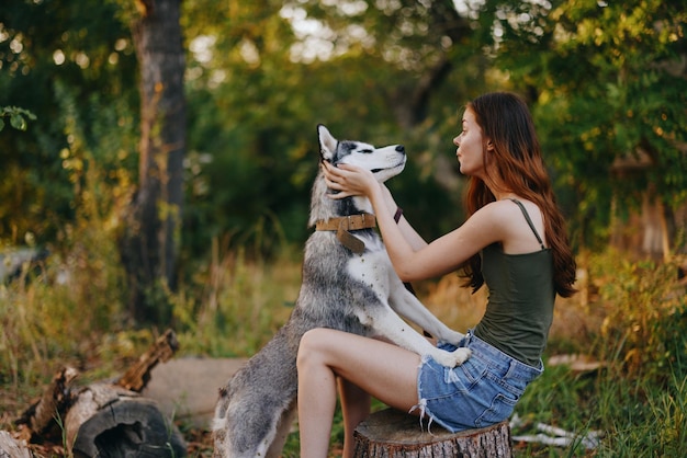 La donna e il suo cane husky giocano felicemente all'aperto nel parco tra gli alberi sorridono con i denti nella passeggiata autunnale con il suo animale domestico