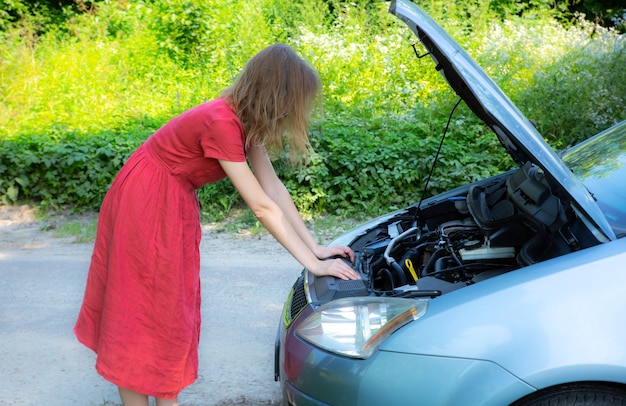 La donna è in piedi vicino all'auto rotta. Situazione di incidente durante il viaggio. La ragazza vestita non sa cosa fare. Aprire il cofano del veicolo.