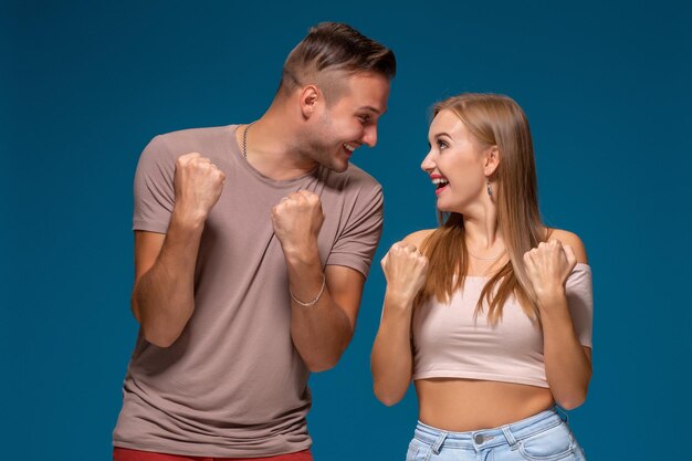 La donna e l'uomo felicissimi alzano i pugni con trionfo, hanno un accordo di successo, esclamano con gioia, su sfondo blu.