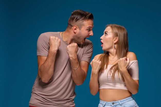 La donna e l'uomo felicissimi alzano i pugni con trionfo, hanno un accordo di successo, esclamano con gioia, su sfondo blu.