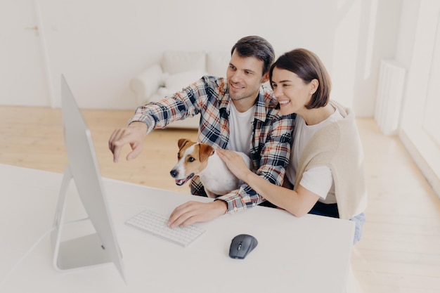 La donna e l'uomo felicissimi hanno un aspetto felice guarda film online a casa insieme giocano con il punto seduto al tavolo bianco cerca informazioni via wifi vestiti con abiti casual Coppia di famiglia naviga in internet