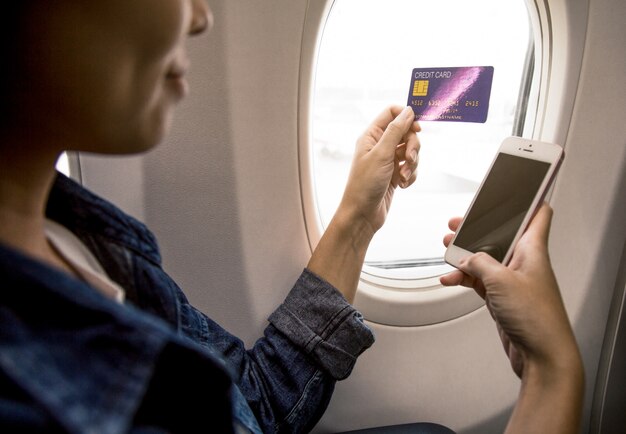 la donna è la mano tiene una carta di credito e uno smartphone sull&#39;aereo.