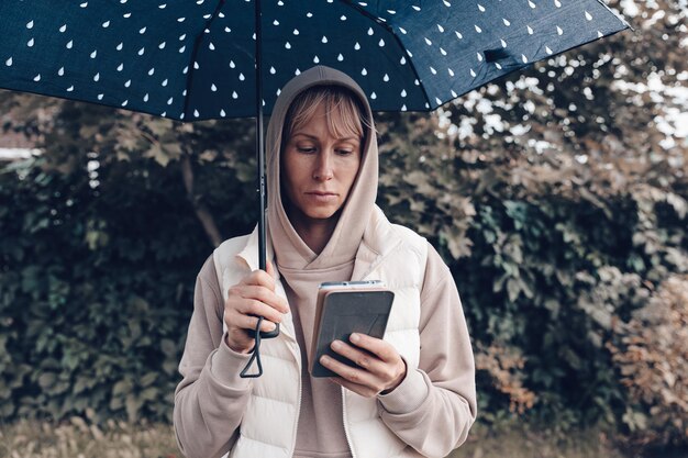 La donna è nel parco autunnale con un ombrello e un telefono Atmosfera autunnale