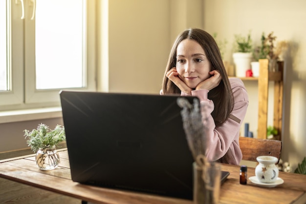 La donna è seduta davanti allo schermo di un computer in un'atmosfera tranquilla e piacevole e ascolta attentamente un video di formazione o una sessione online o semplicemente comunica con un amico